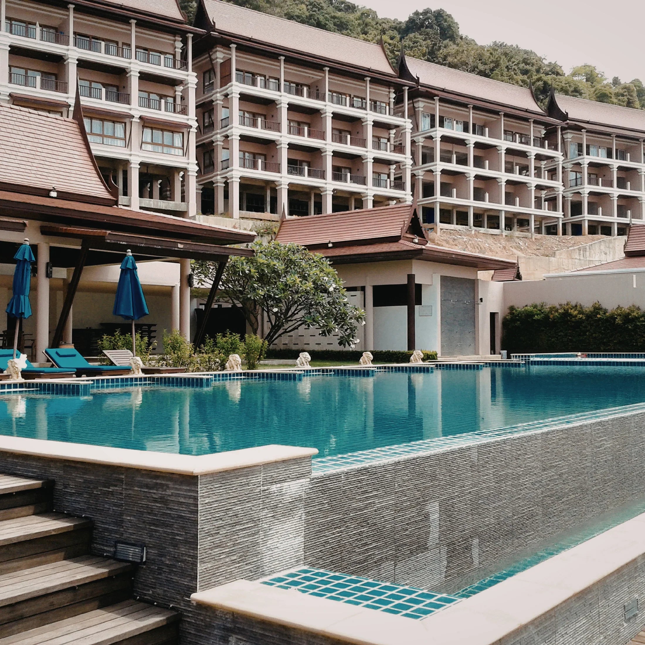 Luxury hotel with infinity pool, lounge chairs, umbrellas, and modern tropical architecture