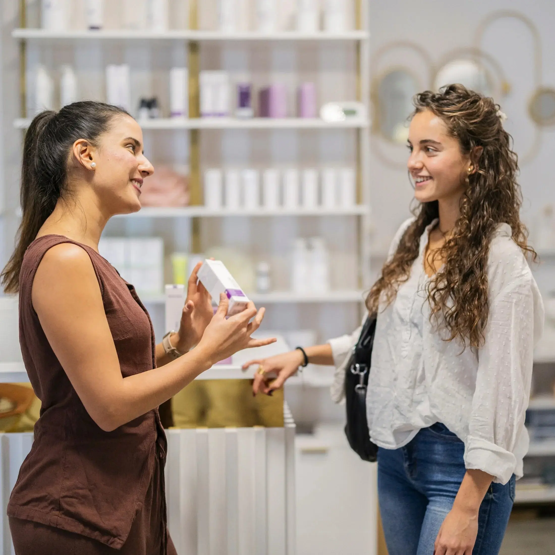 Two women discussing skincare products in a modern wellness store with shelves of cosmetics.