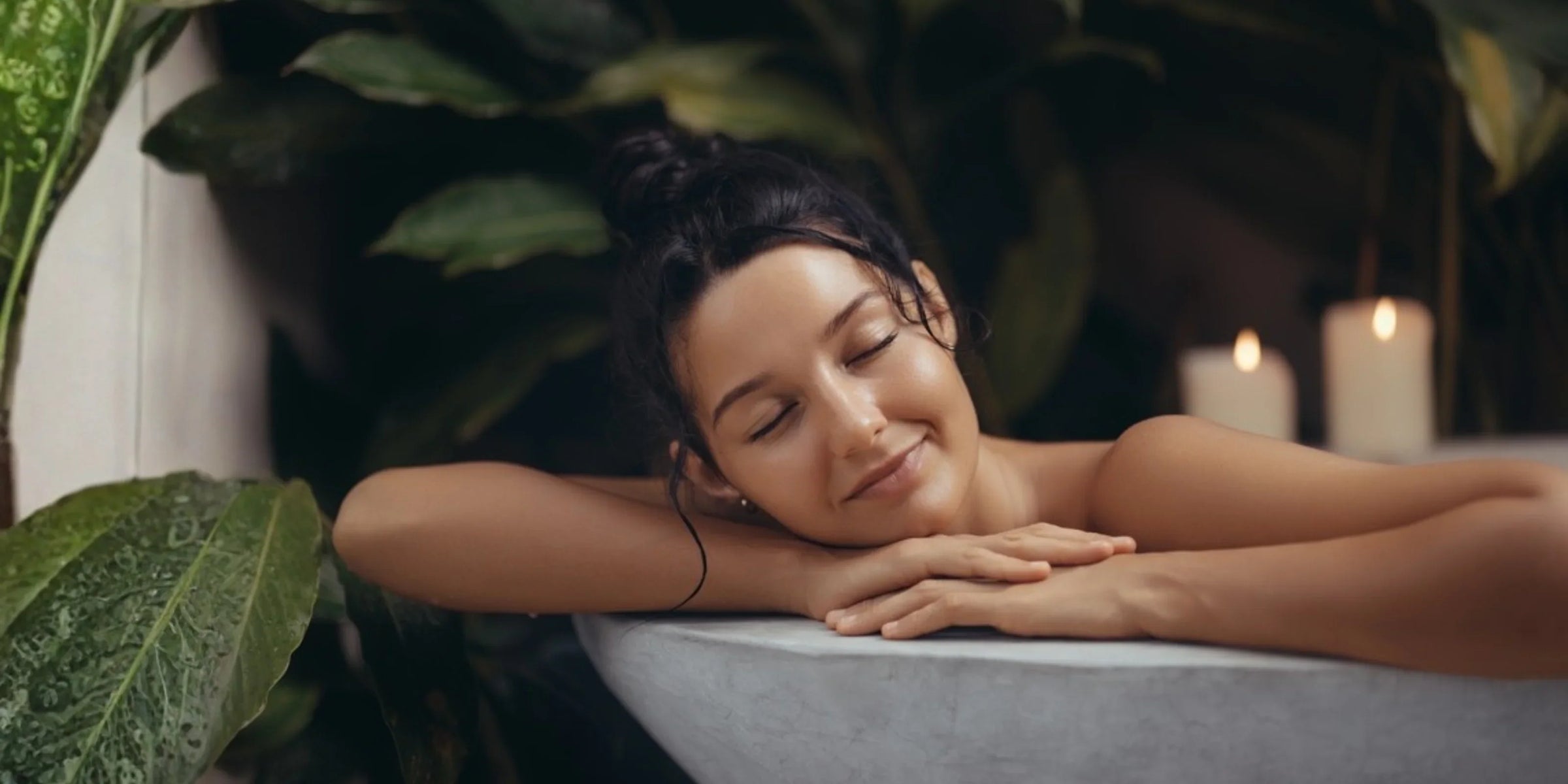 Woman relaxing in a spa bath with candles and lush greenery, promoting wellness and skincare